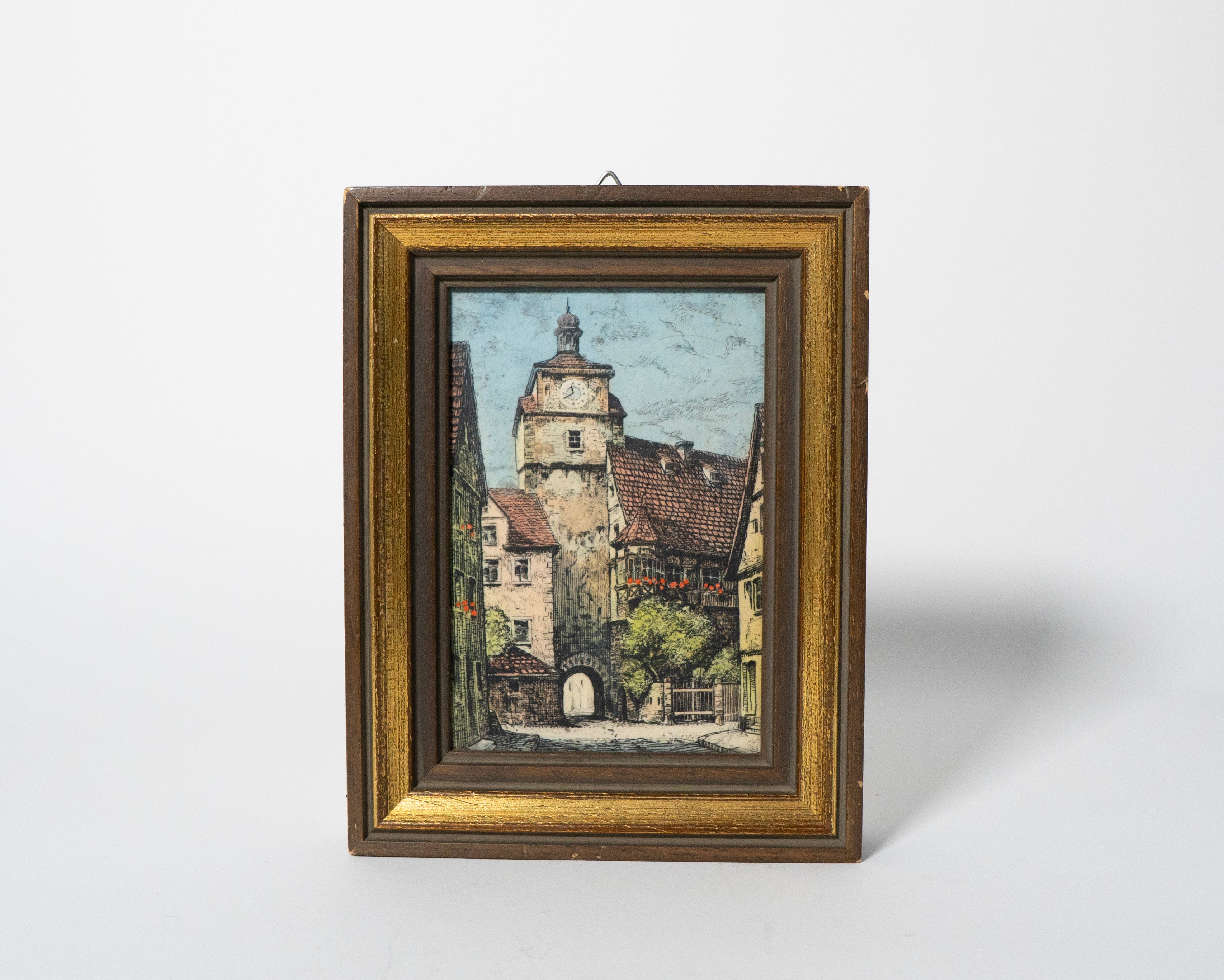 Framed painting of a village scene with a tower on a white background