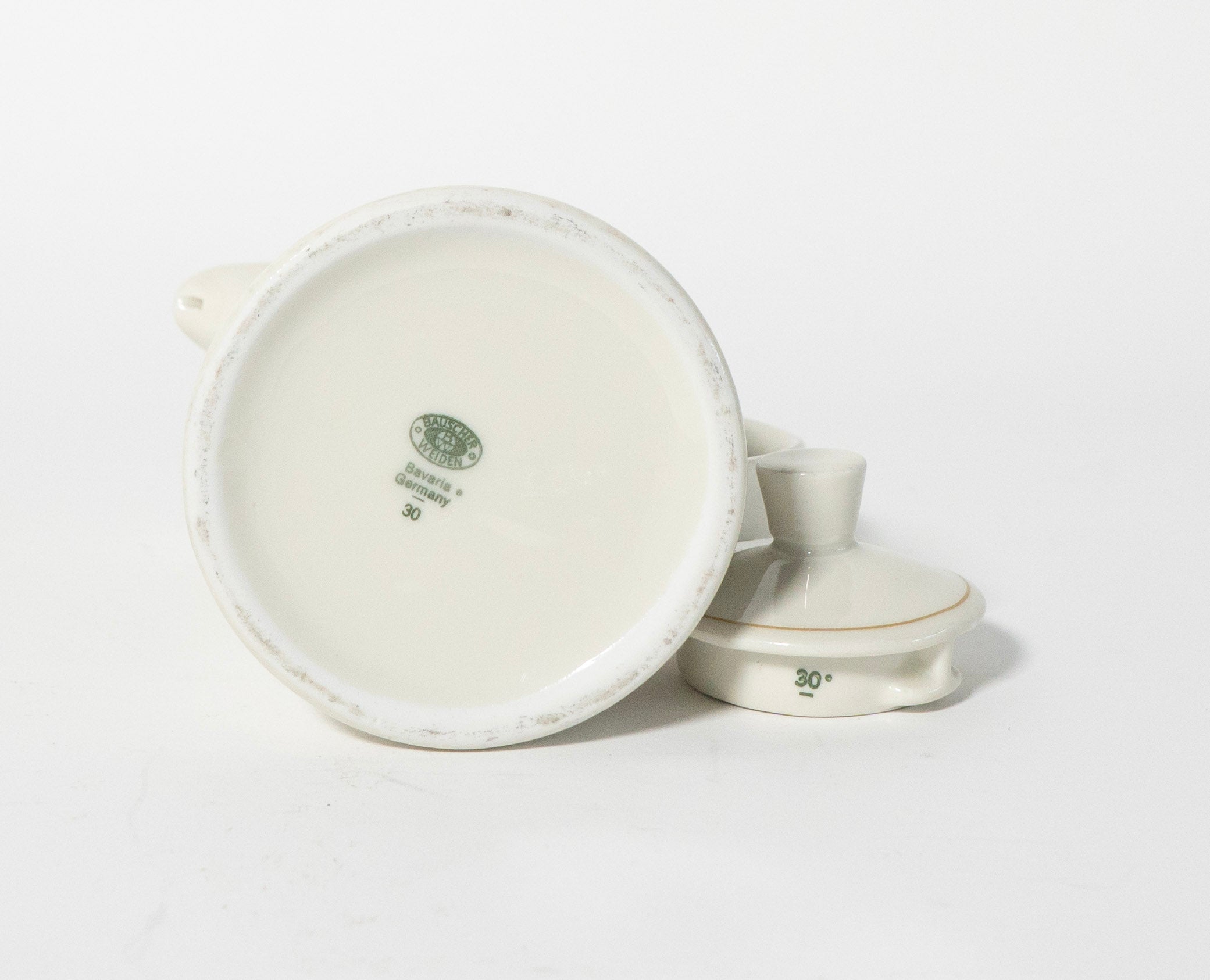 Bottom of white ceramic coffee pot with gold accents and lid on a light gray background