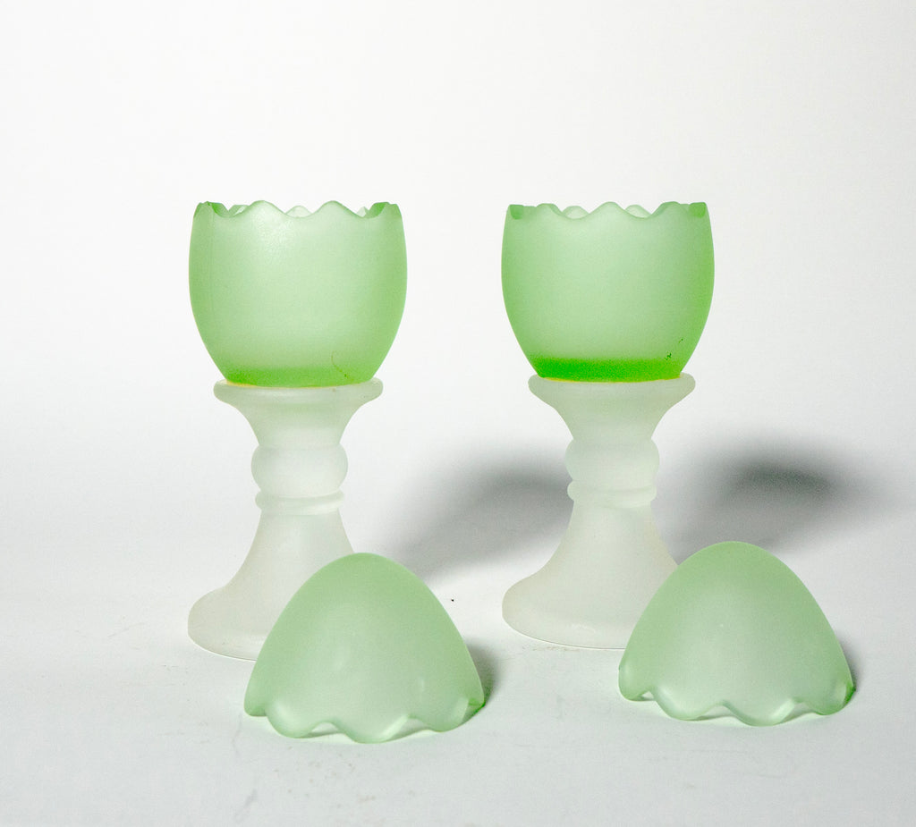 Two green glass egg cups on a white background