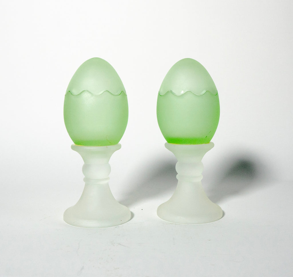 Two green glass eggs on white stands against a white background