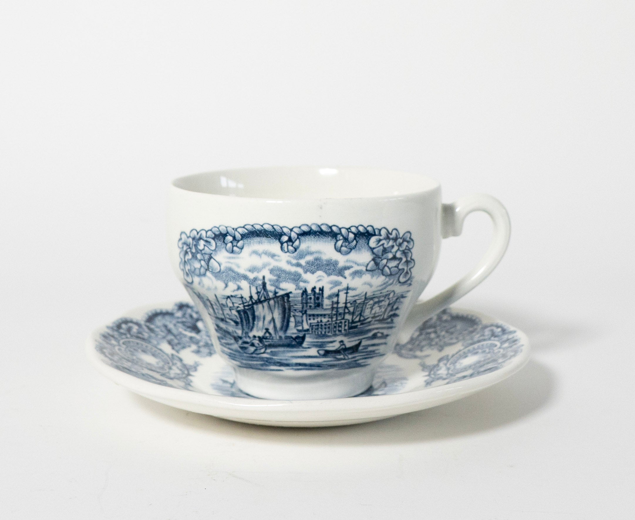 White teacup and saucer with blue boat design on a white background