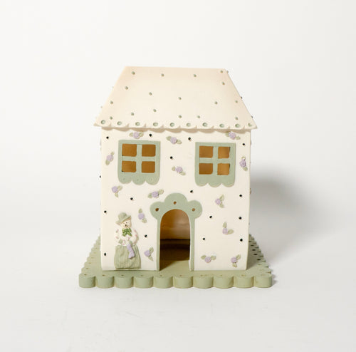 Candle tealight house with a white roof and green base with small snowman next to door on a white background