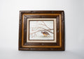 Framed artwork of a bird on a branch with a wooden frame.