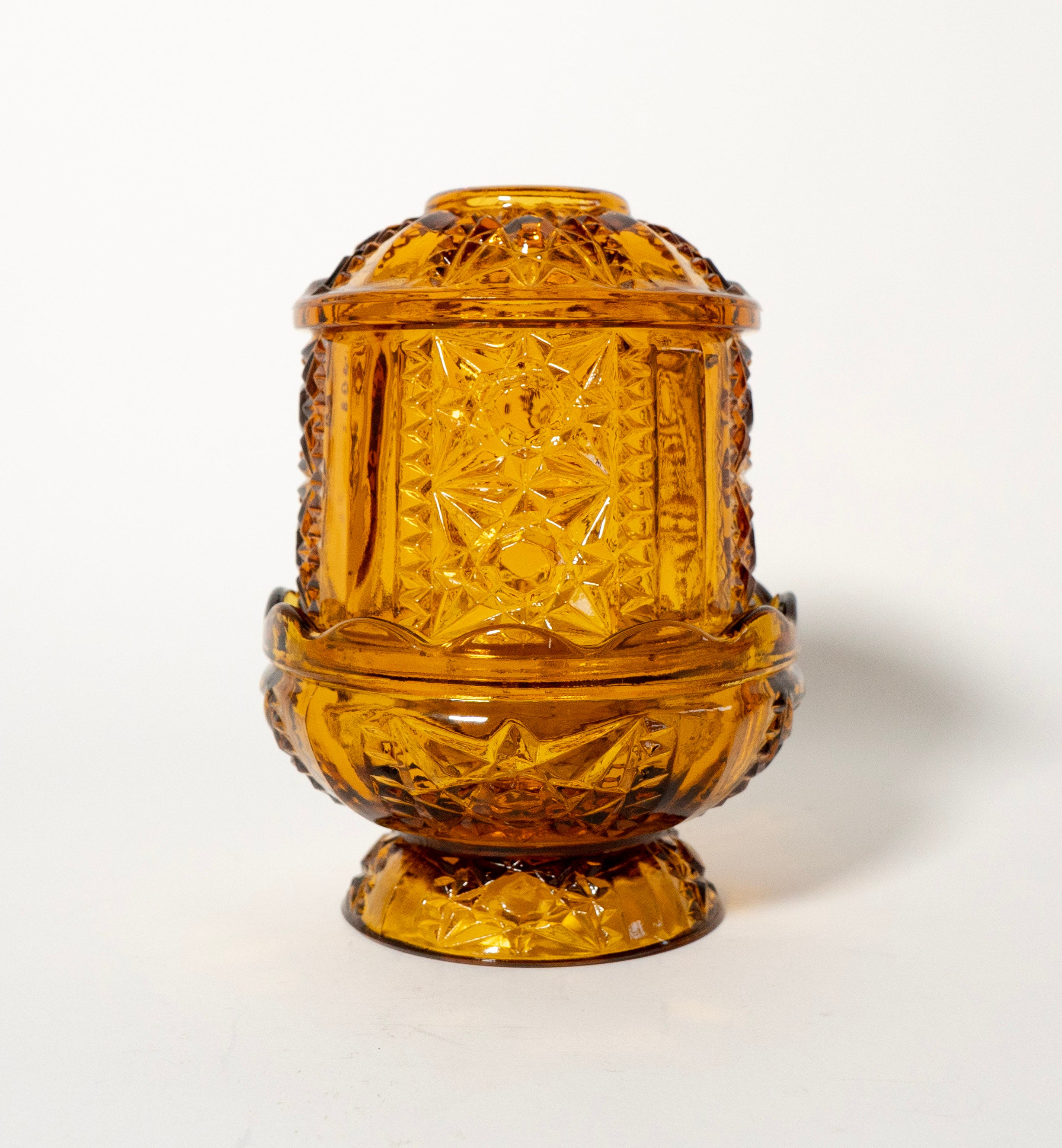 Decorative amber glass candle holder with intricate cut patterns on a white background