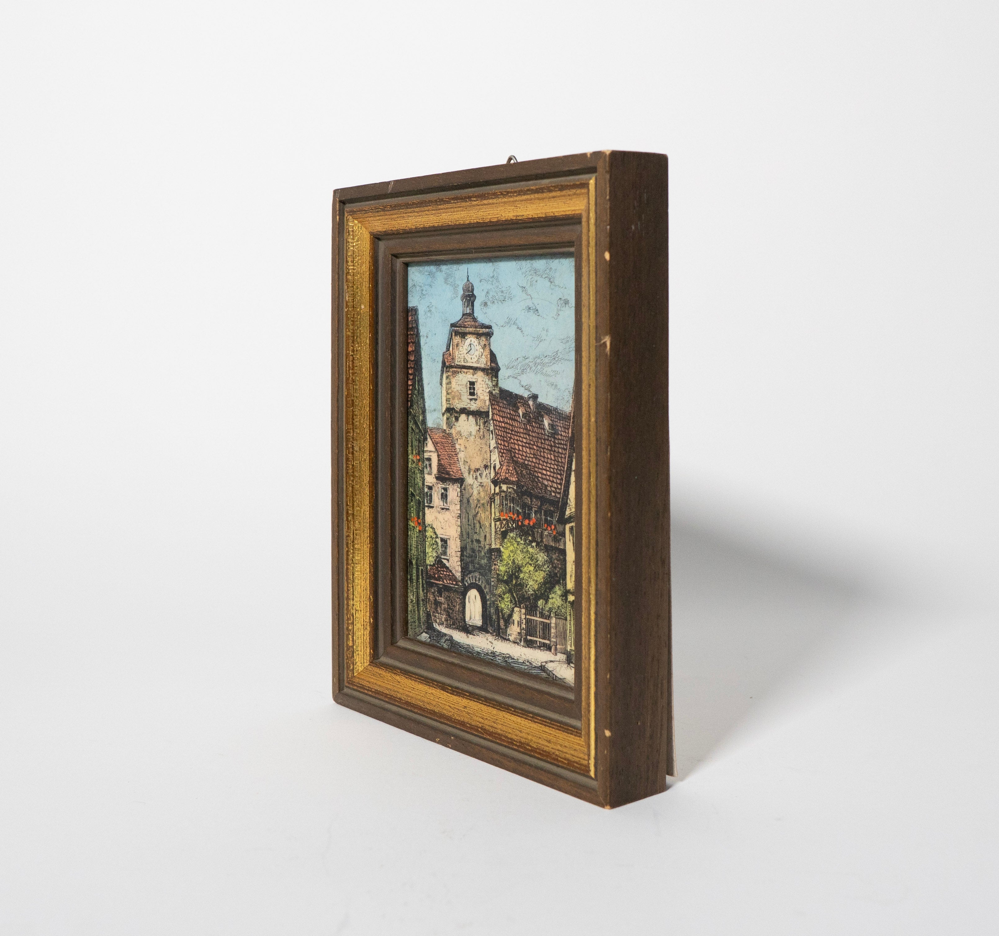 Framed artwork of a village scene with a clock tower on a white background